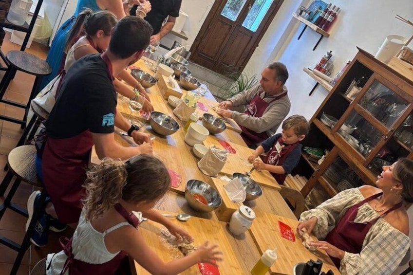 A group of people engaged in a cooking activity around a wooden table with various kitchen utensils and ingredients. 2