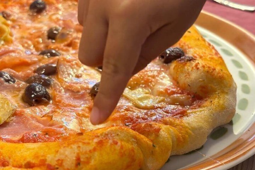 A pizza with toppings and a hand reaching for a slice. 1