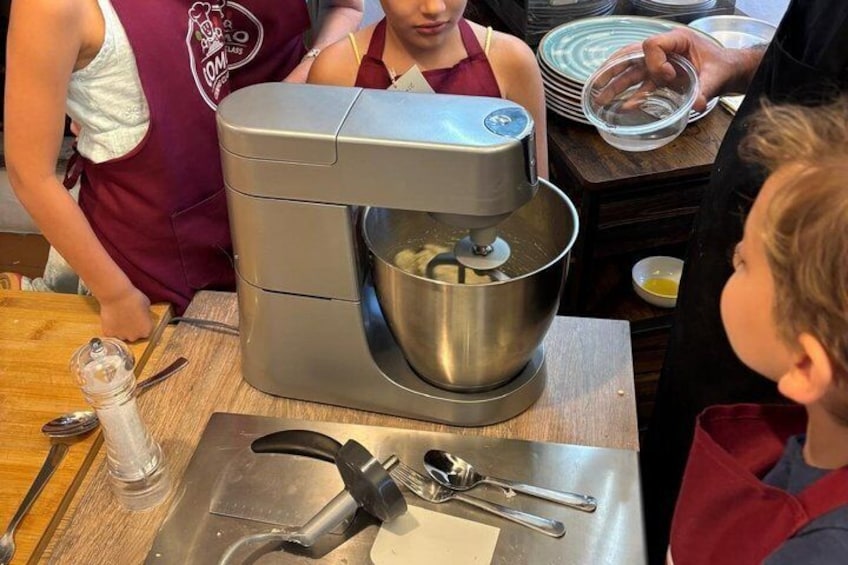 A kitchen with a stand mixer, a child observing, and a woman in a red apron. 4
