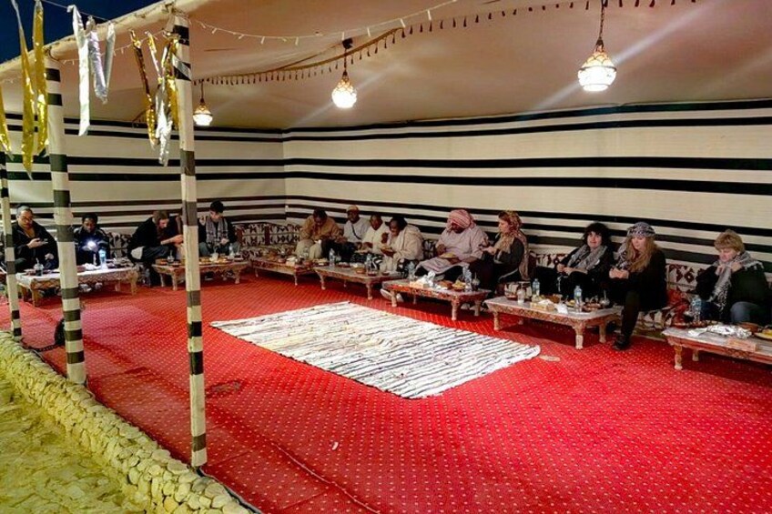 A group of people seated at tables under a striped tent with a red carpet. 2