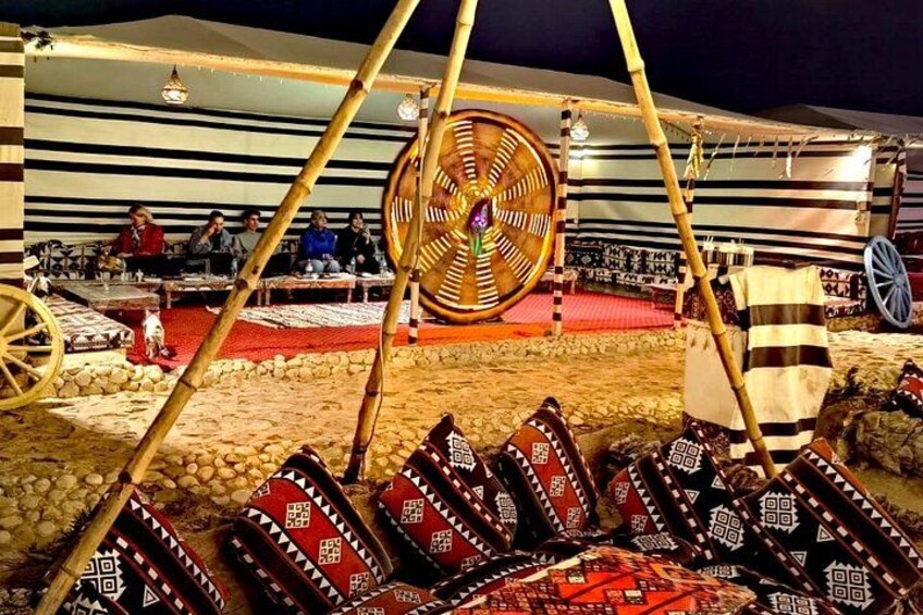 A traditional tent with a spinning wheel, patterned cushions, and a stone-paved ground. 5