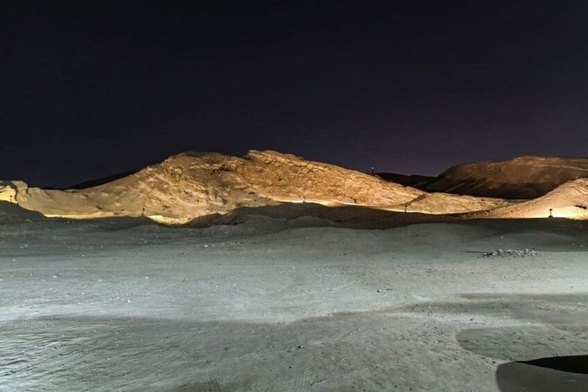 A desert landscape at night with illuminated hills and a flat, rocky foreground. 4