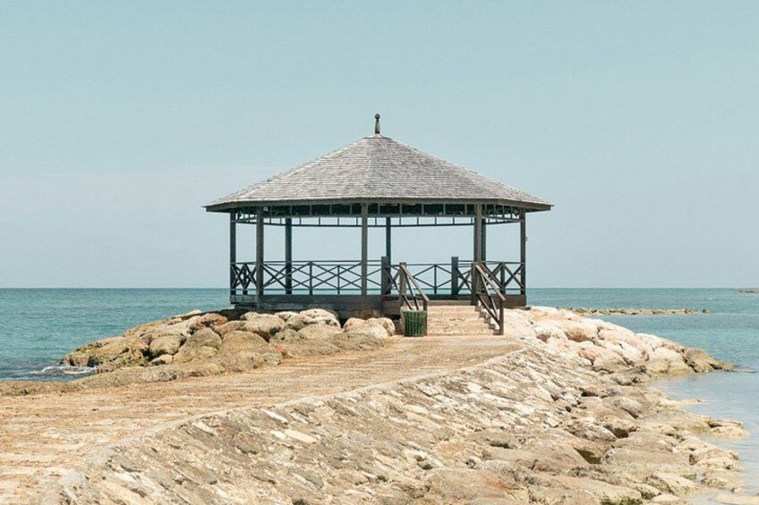 A gazebo on a rocky shoreline with a clear sky. 1