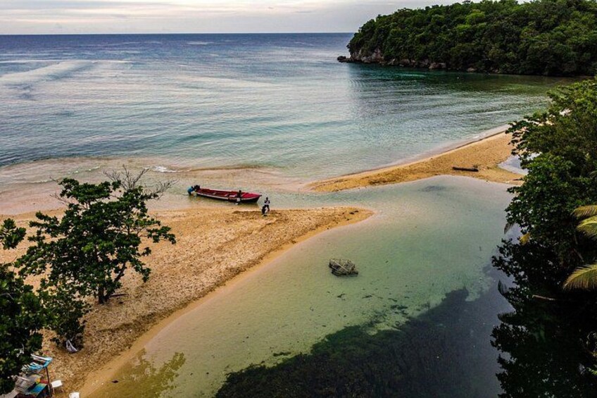 A beach with a boat, clear water, and a forested island. 4