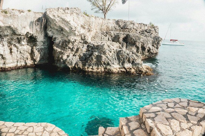 A rocky coastline with clear turquoise water, a boat in the distance, and a stone pathway leading to the water. 3