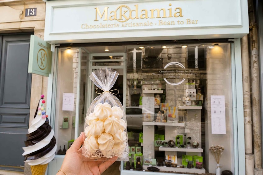 A storefront with a sign reading 'Madamia Chocolaterie artisanale - Bean to Bar' and a hand holding a bag of white chocolate. 2