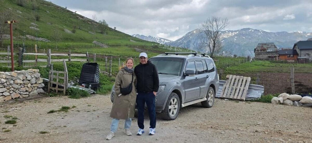 A rural landscape with a stone wall, a parked SUV, and a wooden fence. 4