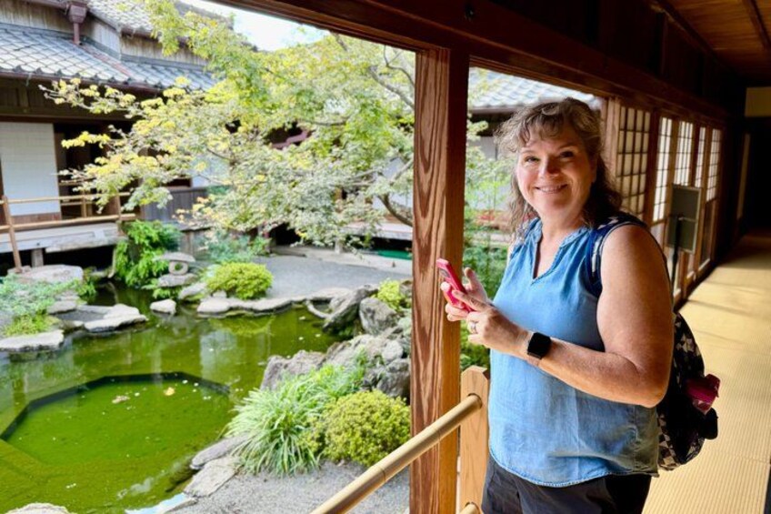 A person standing by a traditional Japanese garden with a pond, rocks, and greenery. 2