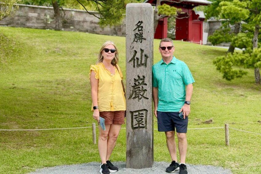 Two people standing next to a stone marker with Japanese characters. 3