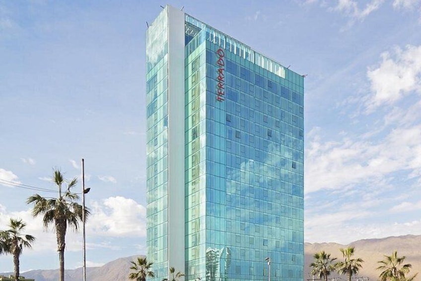 A modern glass building with the name 'TERRADO' on its facade, surrounded by palm trees and mountains in the background. 4