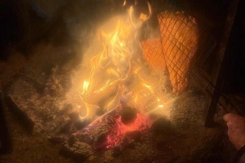 A campfire with a grid-like object over it, possibly a grill, and a person lying down nearby. 2
