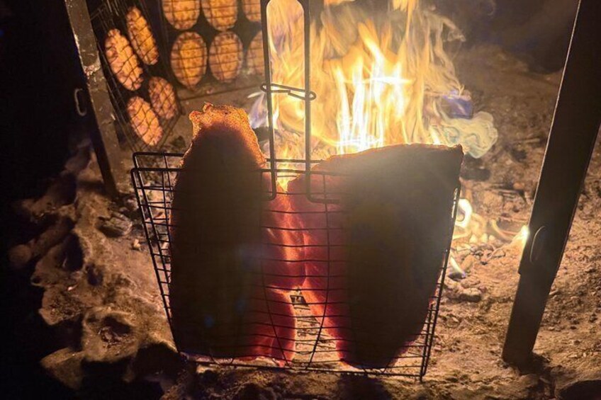 A grill with two pieces of meat cooking over an open fire. 3