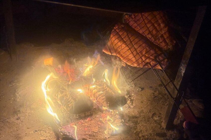 A campfire with burning logs and a metal grill with food. 4