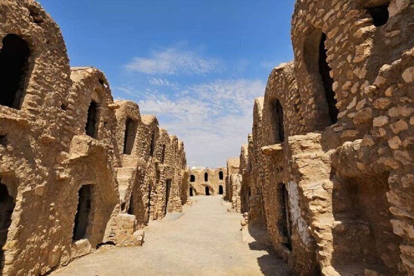 A pathway flanked by ancient stone buildings with arched windows and doorways. 1