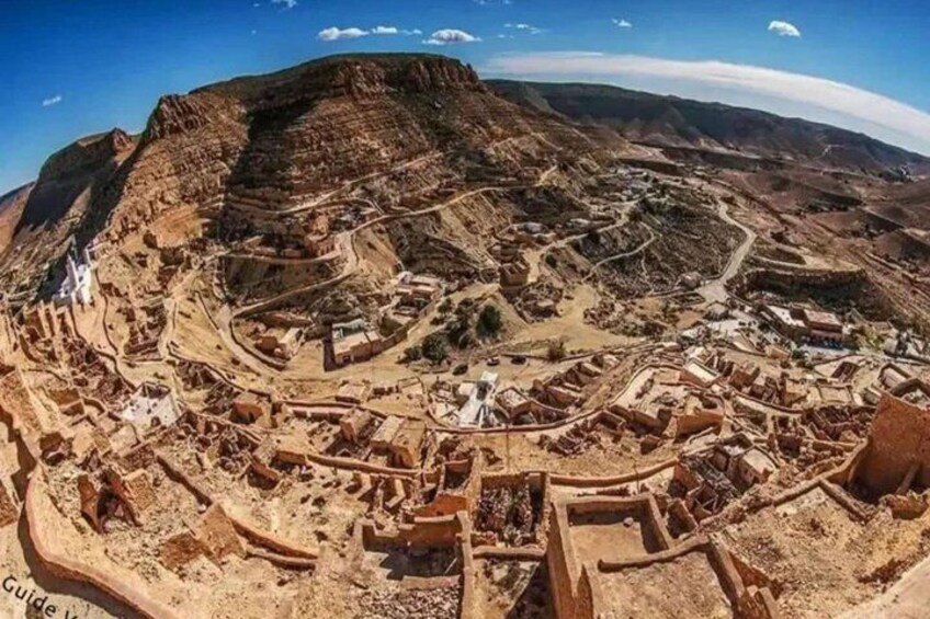 A panoramic view of an ancient city with winding roads, terraced structures, and a prominent mountain in the background. 3
