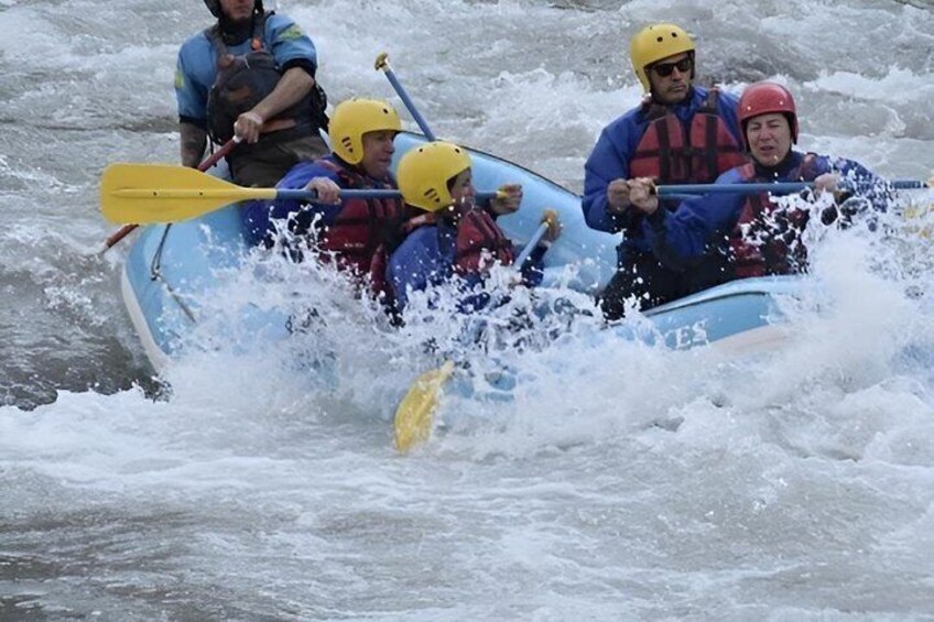 A group of people in a blue inflatable raft navigating through rough waters. 3