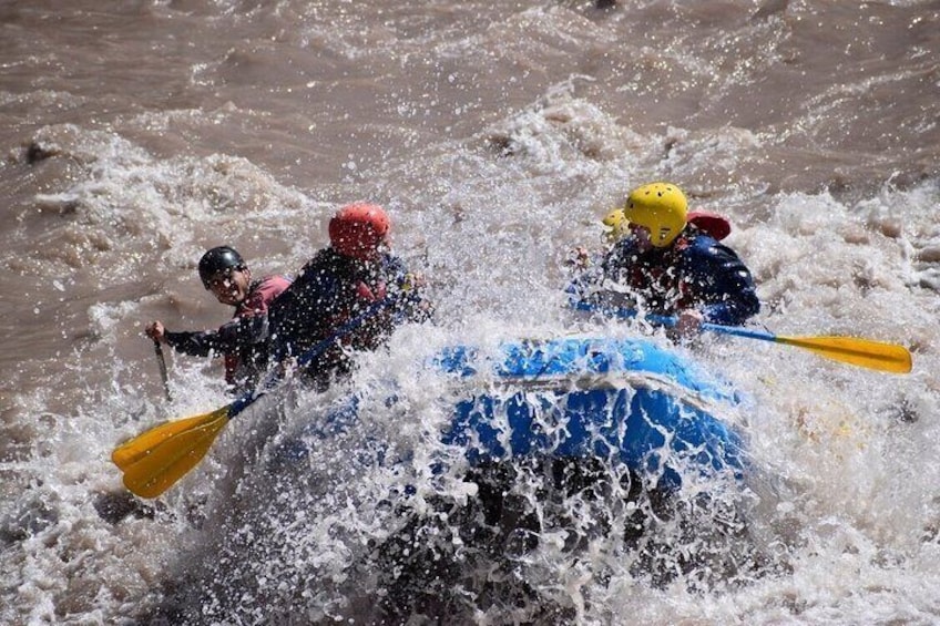 People in a blue raft navigating through turbulent water. 5