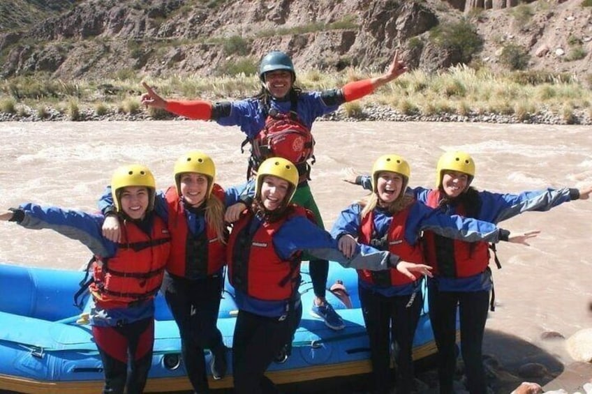 A group of people wearing helmets and life jackets on a raft. 1
