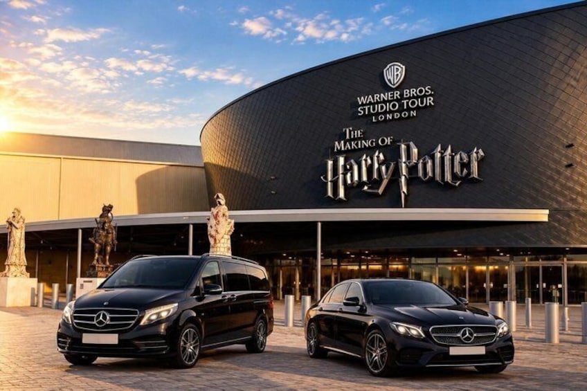 A building with a Warner Bros. Studio Tour sign, two black Mercedes-Benz cars parked in front, and statues on the left. 1