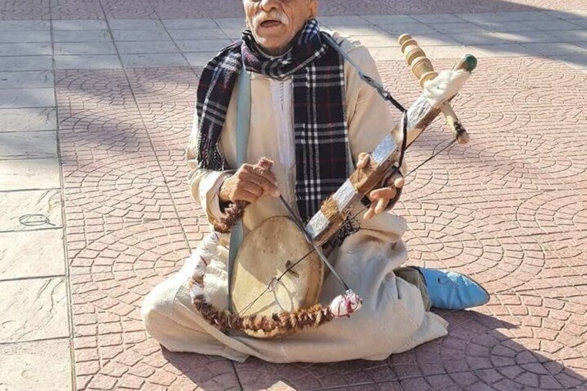 A person sitting on the ground playing a traditional stringed instrument. 3