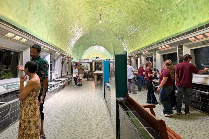 A subway station with tiled walls, benches, and people standing by the platform. 3
