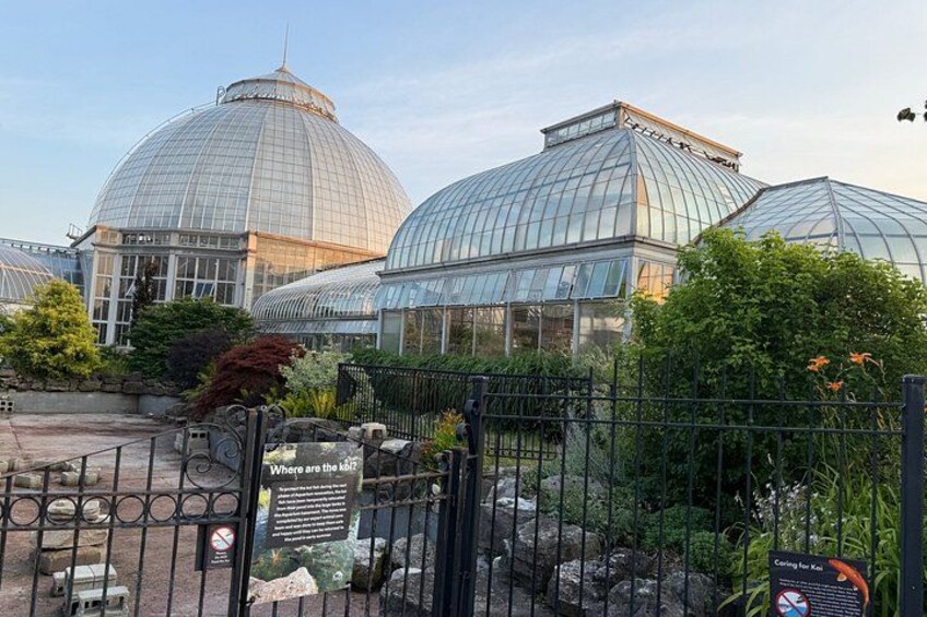 A greenhouse complex with large glass domes, surrounded by a metal fence and various plants. 3