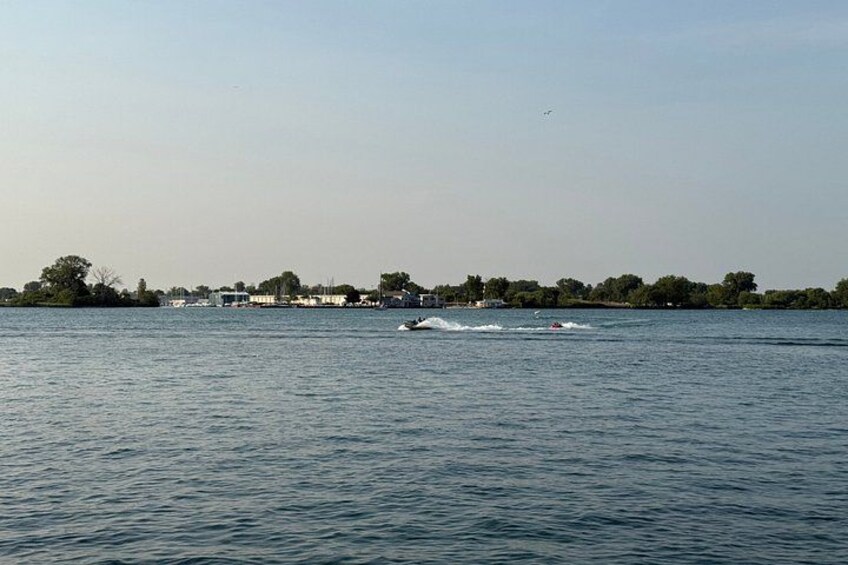 A calm lake with a small boat in the distance, a shoreline with buildings, and a clear sky. 4