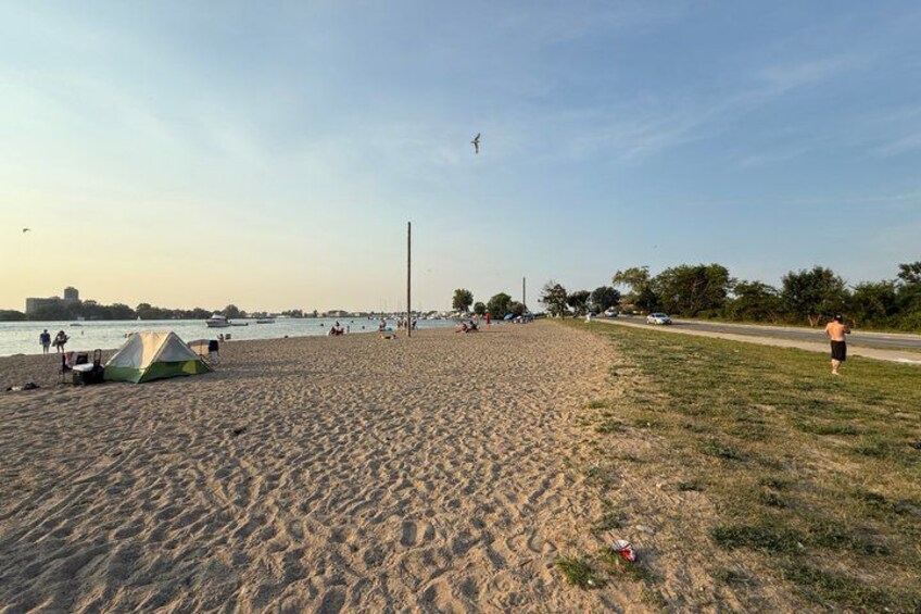 A sandy beach with a tent, a grassy area, and a body of water in the background. 5