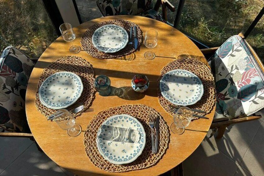 A round wooden table set for four with woven placemats and patterned plates. 4