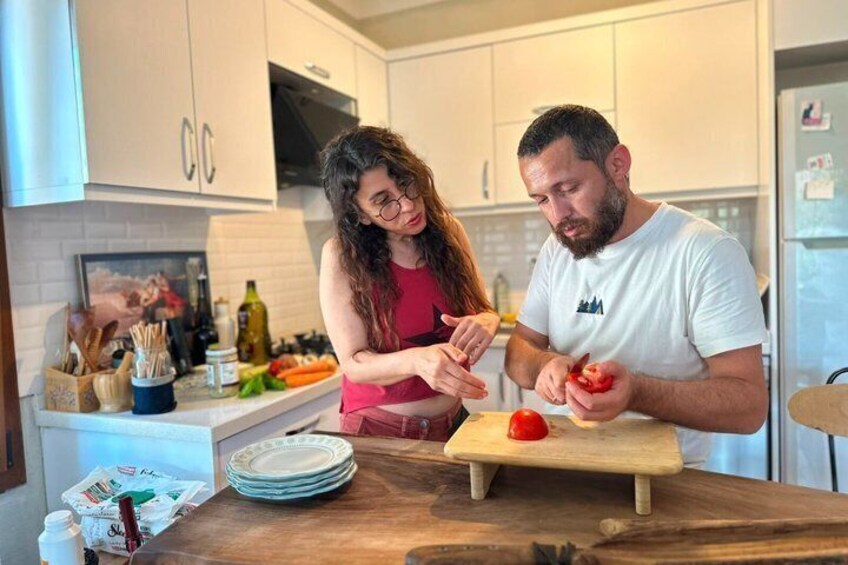 Two people preparing food in a kitchen with white cabinets, a wooden countertop, and various kitchen utensils. 2