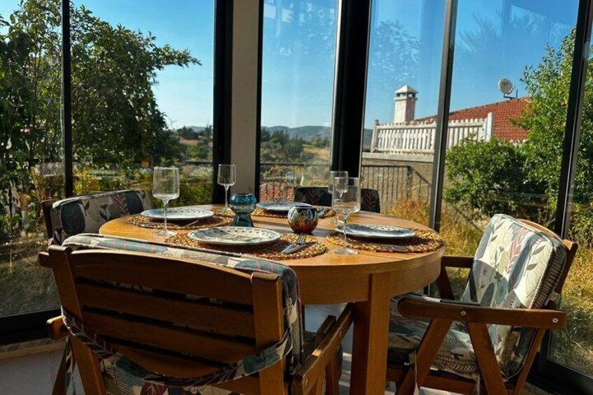 A round wooden table set for dining with chairs, large windows, and a view of a distant building. 3