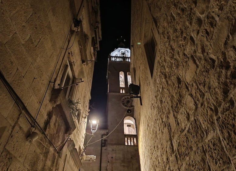 A narrow alleyway with a building featuring a clock tower and arched windows. 3