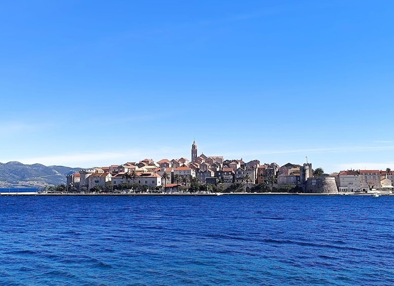 A coastal town with historic buildings, a prominent church, and a clear blue sea. 1
