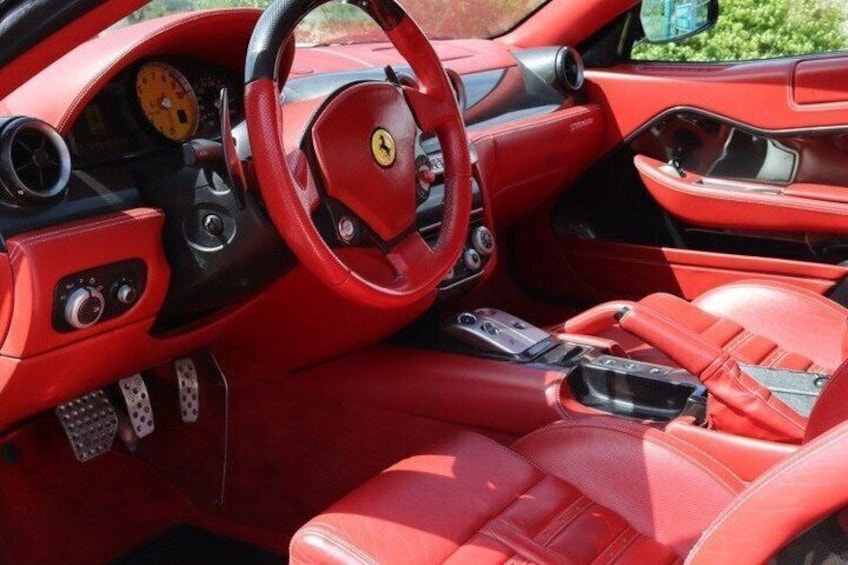 A red Ferrari sports car interior with leather seats, a steering wheel, and a dashboard. 4