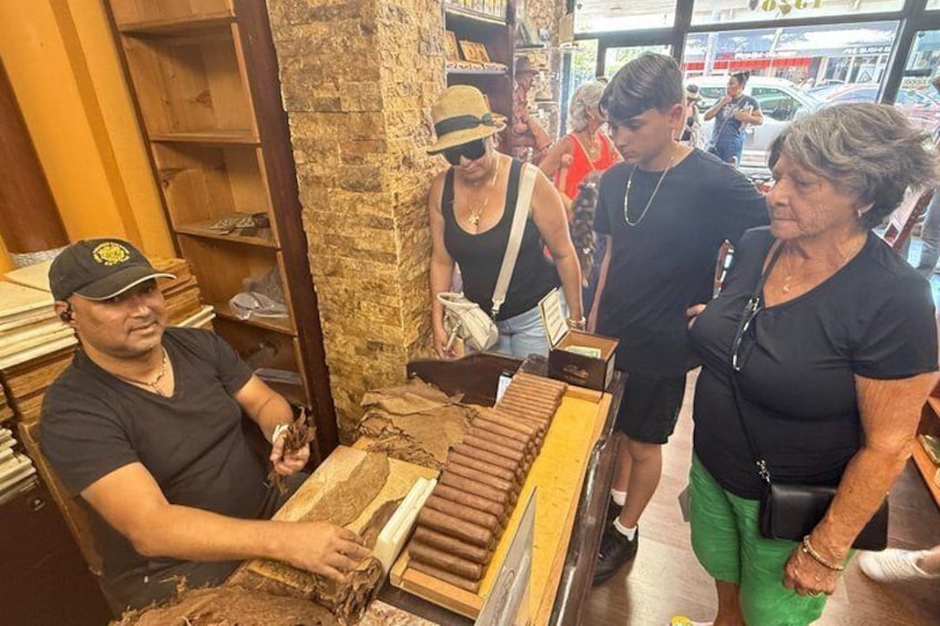 A cigar store with a man rolling cigars, shelves with cigars, and customers browsing. 3