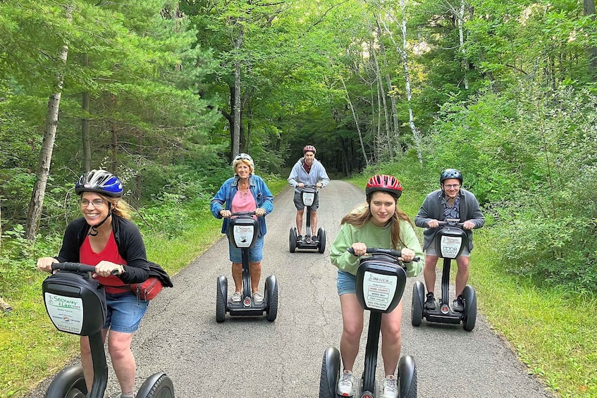 A group of people riding Segway scooters on a gravel path surrounded by trees. 2