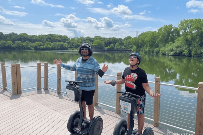 Two people on segways on a wooden dock by a lake with trees in the background. 3