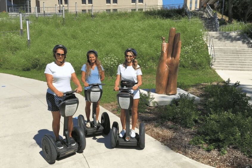 Three people riding segways on a sidewalk with a sculpture and stairs in the background. 2