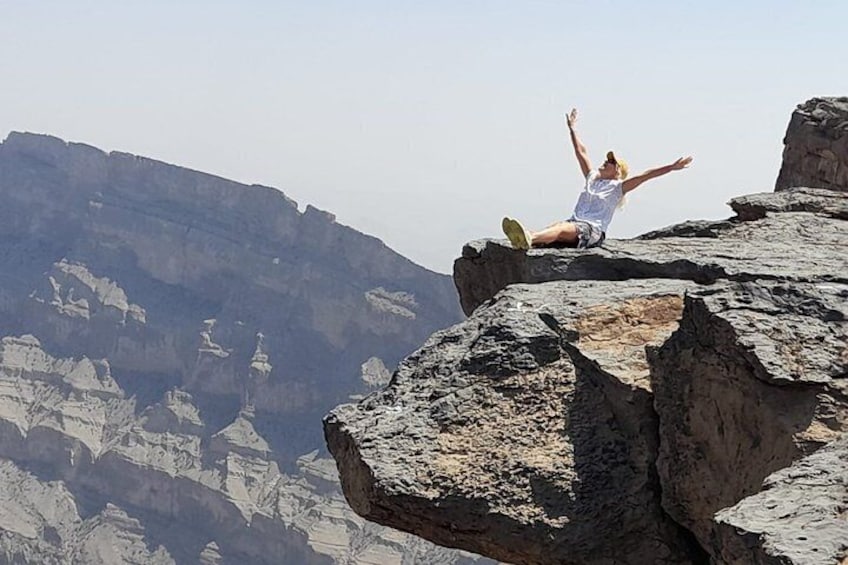 A person sitting on a rock with arms raised, overlooking a mountainous landscape. 5