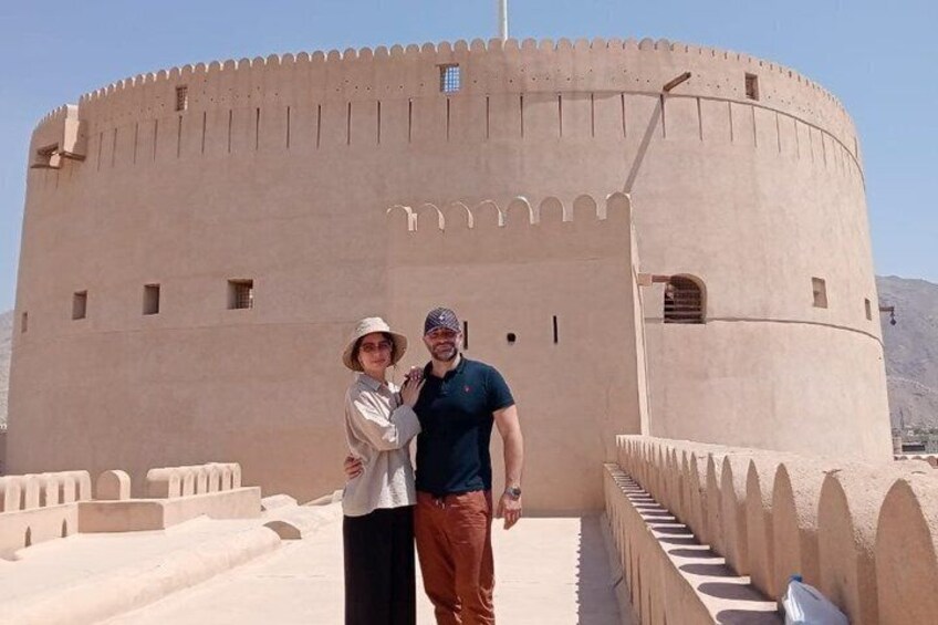 A large, round, beige fortress-like structure with crenellations, a clear sky, and a mountainous backdrop. 4