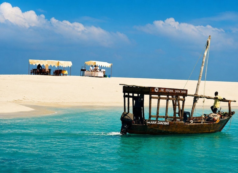 A traditional dhow boat on turquoise water with a sandy beach and two tents in the background. 2