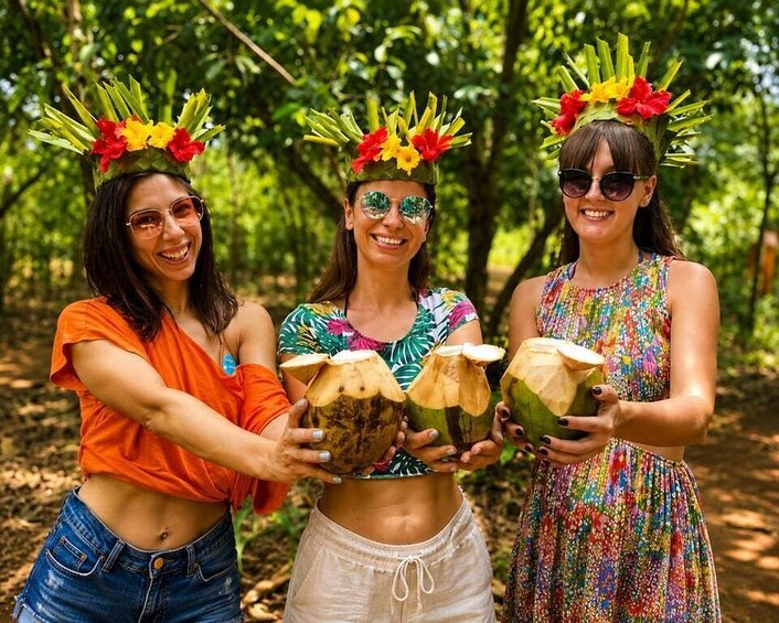 Three people holding coconuts in a forest. 1