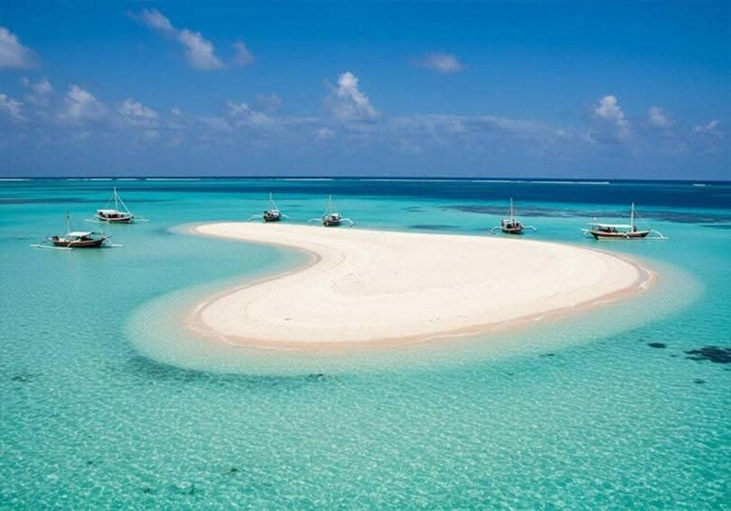 A turquoise lagoon with a white sandy beach, surrounded by small boats anchored in the water. 4