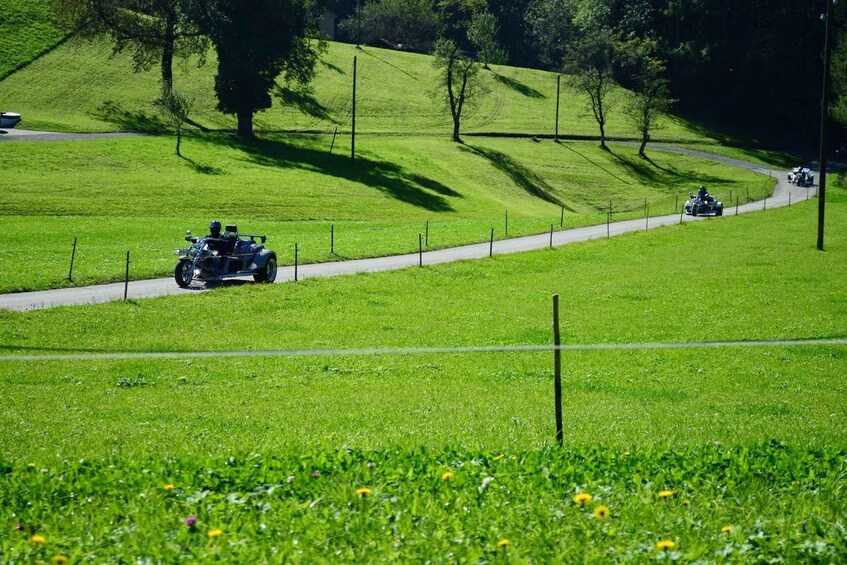 A motorcycle on a paved path in a grassy field with a fence and trees in the background. 1