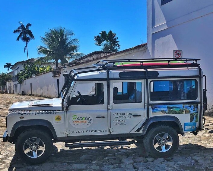 Un vehículo todoterreno blanco estacionado en una calle adoquinada, con palmeras y un edificio al fondo. 3