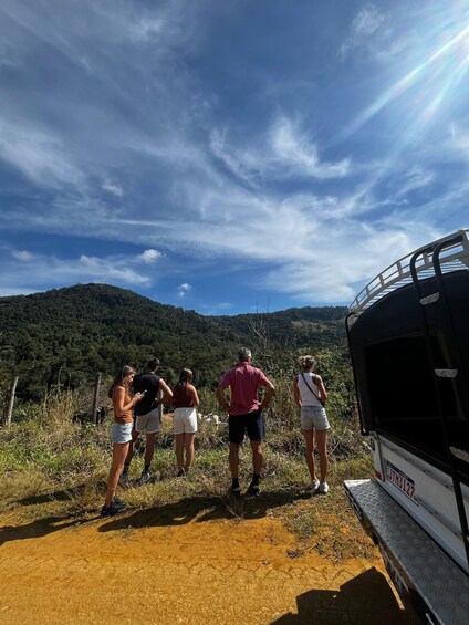 Un groupe de personnes se tient sur un chemin de terre, à proximité d’un véhicule garé, et surplombe un paysage vallonné. 4