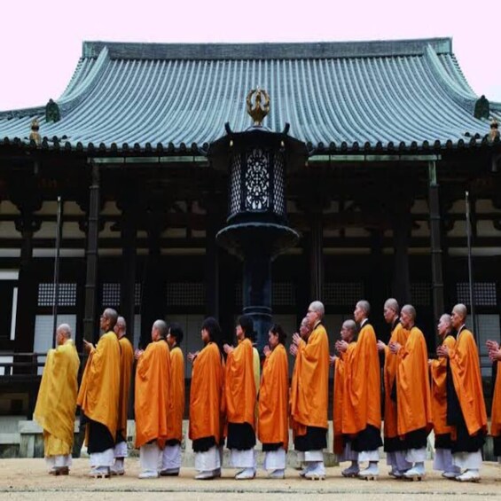 Monks in orange robes walking in front of a traditional building with a green roof. 5