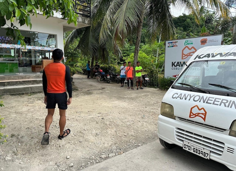 A white van with 'CANYONEERING' and 'KAWANA' logos parked on a dirt road, surrounded by greenery and people. 5