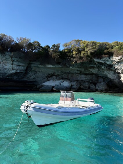 A small boat anchored near a rocky cliff with clear turquoise water. 3