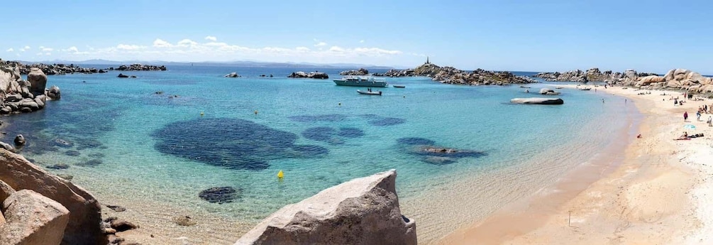 A coastal beach with clear turquoise waters, rocky outcrops, and a few boats. 4